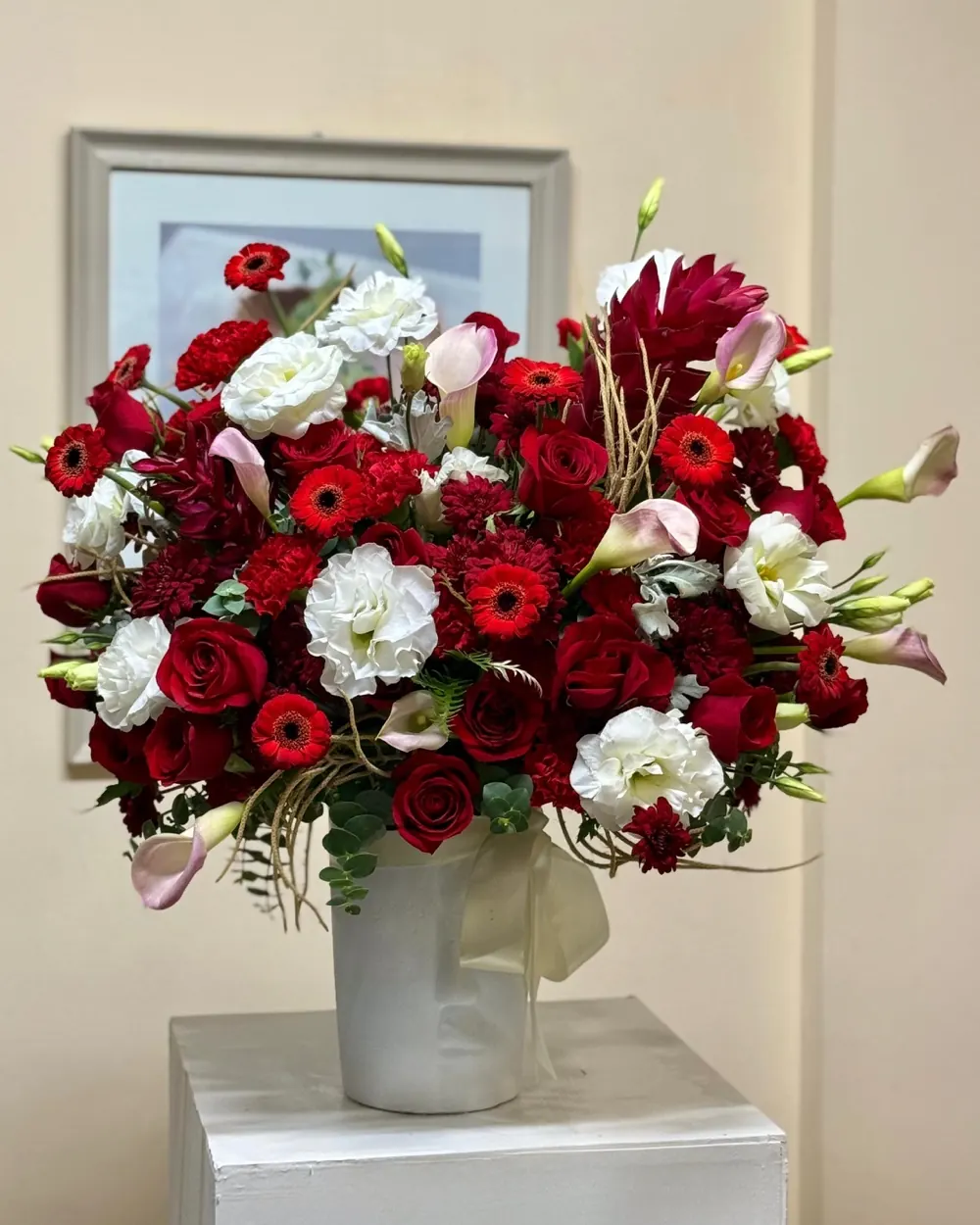 Arreglo de rosas rojas, gerberas y lisianthus blancos en jarrón blanco