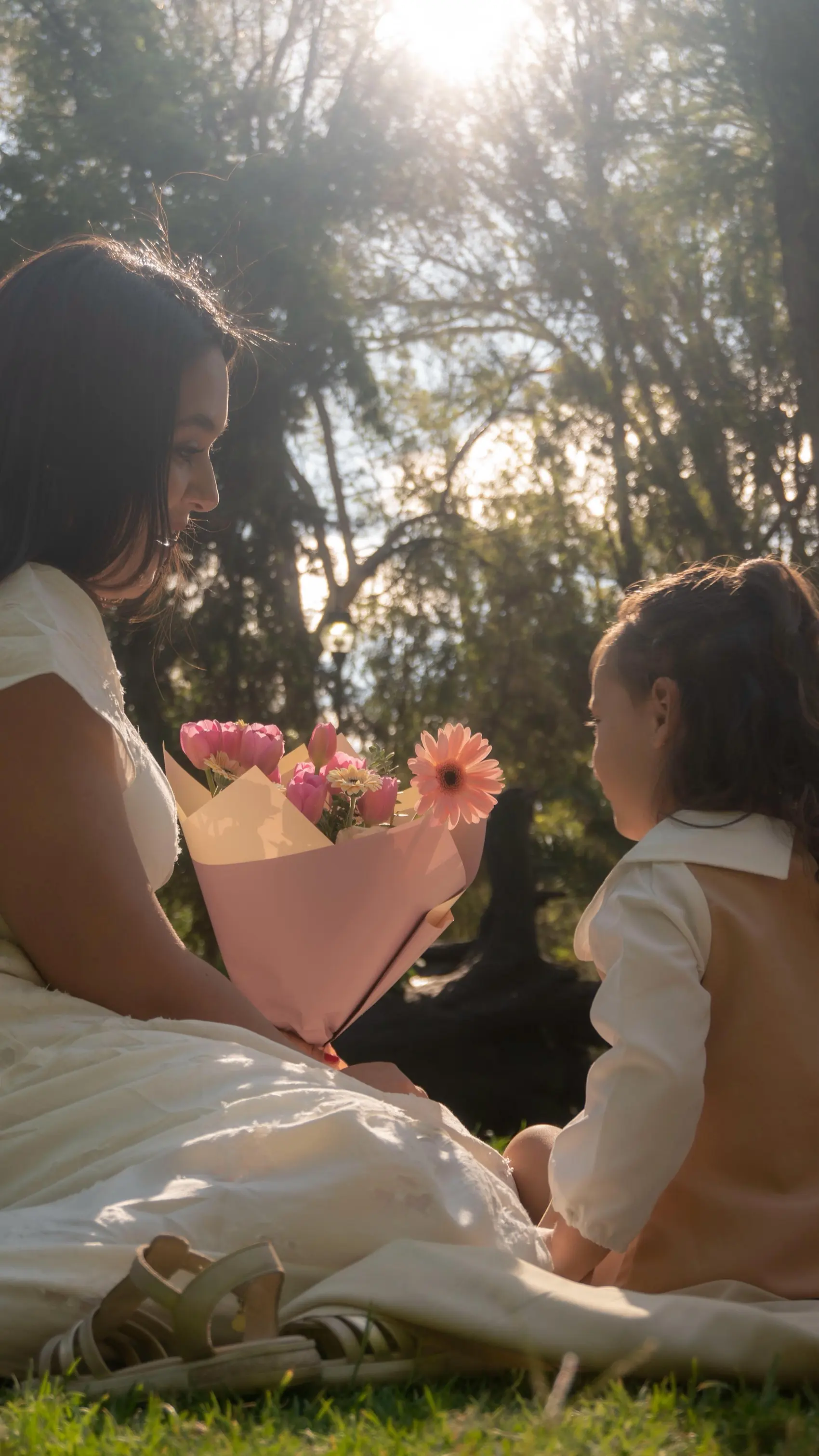 Una mamá le entrega un ramo de tulipanes a su hija en el parque, a contraluz